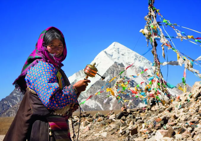 Moulin à prières dans la main, une pèlerine bouddhiste s’est arrêtée devant les petits drapeaux sur lesquels les Tibétains écrivent des invocations que le vent emporte vers les divinités. © Christopher Tozer/Alamy Stock Photo