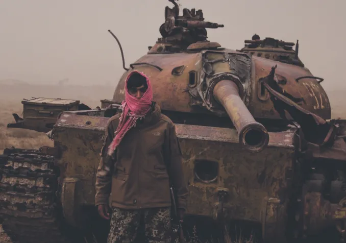 Août 2021, dans un faubourg de Kaboul (Afghanistan), un homme armé pose devant une épave de tank taliban. ©iStock/Trent Inness